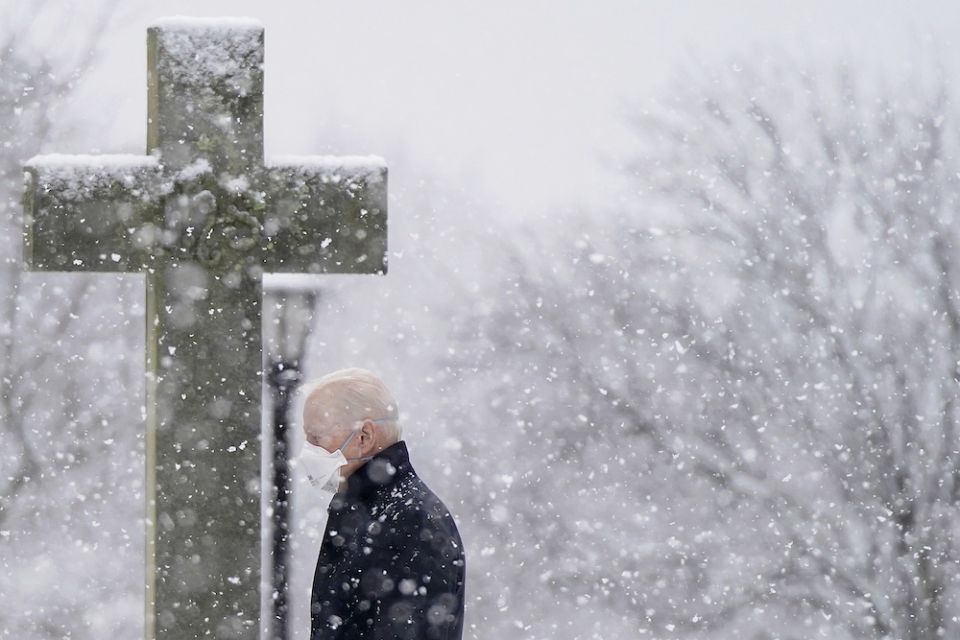 stone cross in churchyard in the snow as President Joe Biden walks by in a mask