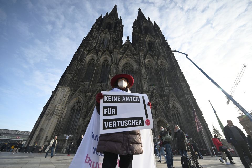 A participant of a rally of the initiative Maria 2.0 holds a poster with the inscription 'No offices for cover-ups' in front of the cathedral in Cologne, Germany, Thursday, Nov. 18, 2021. (Henning Kaiser/dpa via AP)