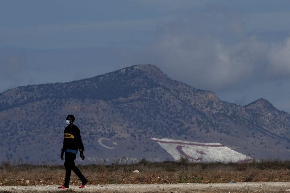A migrant walks near Pournara migrant reception center in Kokkinotrimithia, as a giant Turkish Cypriot breakaway flag, right, and Turkish flags painted on a mountain are seen in the background in the Turkish occupied area of the ethnically divided island 