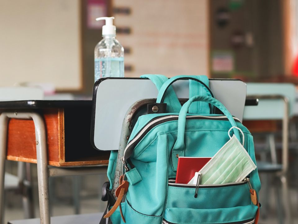 A disposable face mask is seen in a backpack hanging on a school desk holding a bottle of hand sanitizer. (Dreamstime/Phuttharak Chindarot) A disposable face mask is seen in a backpack hanging on a school desk holding a bottle of hand sanitizer. (Dreamstime/Phuttharak Chindarot)