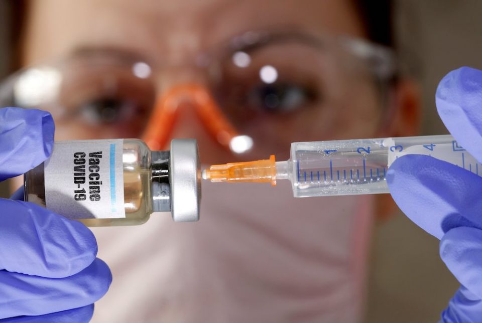 A woman holds a small bottle labeled with a "Vaccine COVID-19" sticker and a medical syringe in this photo illustration. (CNS Illustration/Reuters photo/Dado Ruvic)