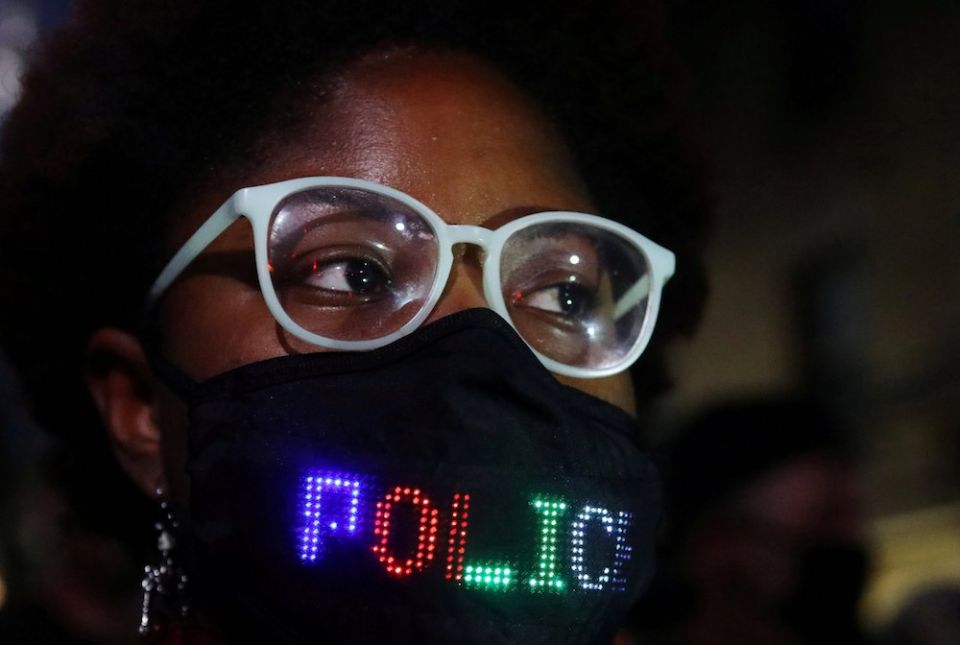 A person in a mask with lights spelling out at least the word "police" stands outside the site of the 2020 vice presidential debate between Vice President Mike Pence and Democratic vice presidential nominee Sen. Kamala Harris on the campus of the Universi