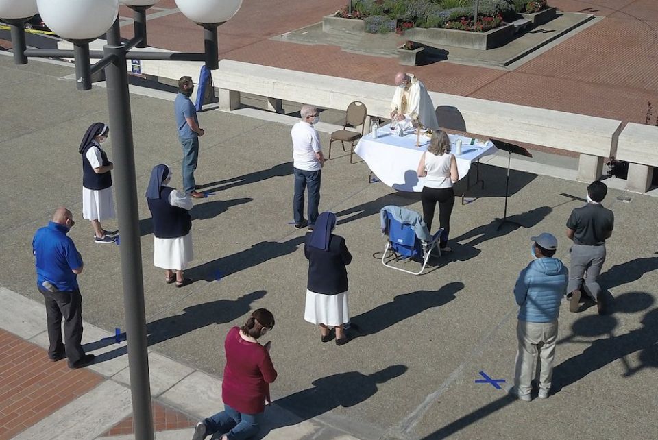 Jesuit Fr. John Piderit, San Francisco's archdiocesan vicar for administration, celebrates Mass simultaneously with three other priests on the feast of the Assumption near the steps of the city's Cathedral of St. Mary of the Assumption Aug. 15, 2020. (CNS People standing outside socially distanced while a priest celebrates Mass