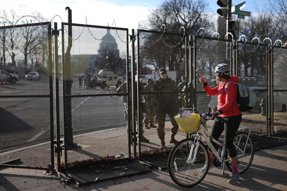 The U.S. Capitol can be seen behind the protective fence line Jan. 21, 2021, as a cyclist talks to a U.S. National Guard member inside. (CNS/Reuters/Tom Brenner)