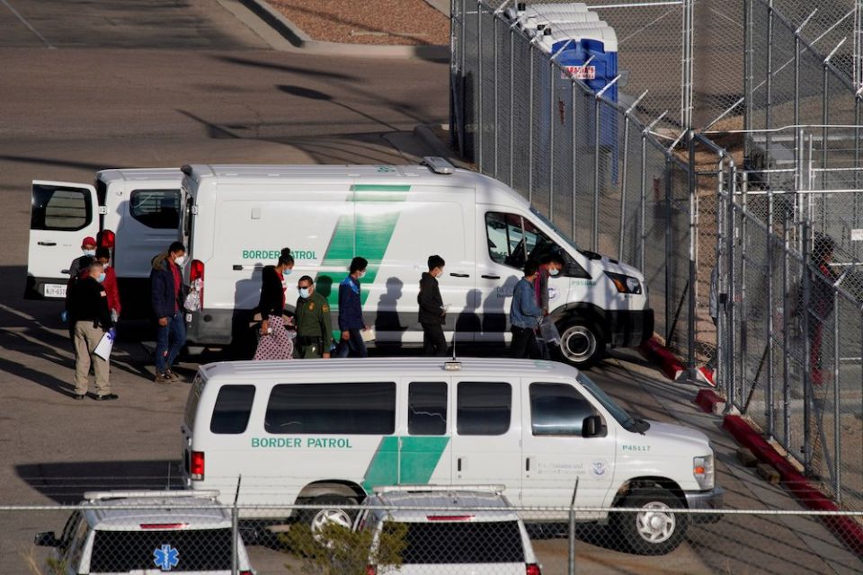 Vans from Border Patrol parked at a fence while people get out and walk