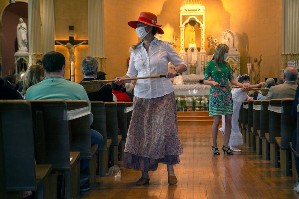 Two women walking down church aisle with long handled collection baskets