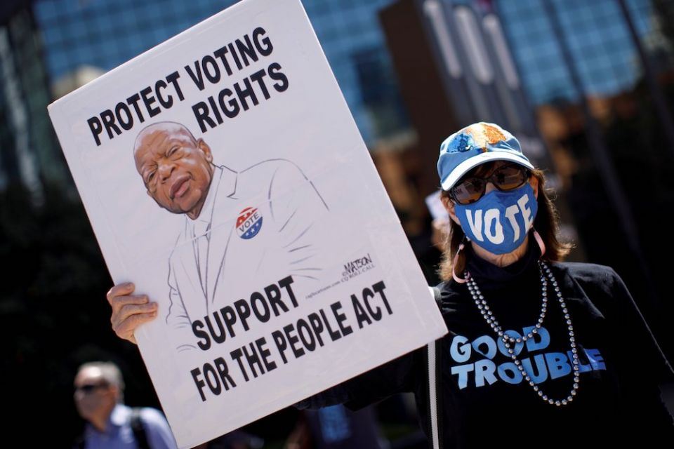 person in a "vote" mask holding a placard April 5, 2021, with U.S. Rep. John Lewis and the words "Protect Voting Rights, Support For the People Act"