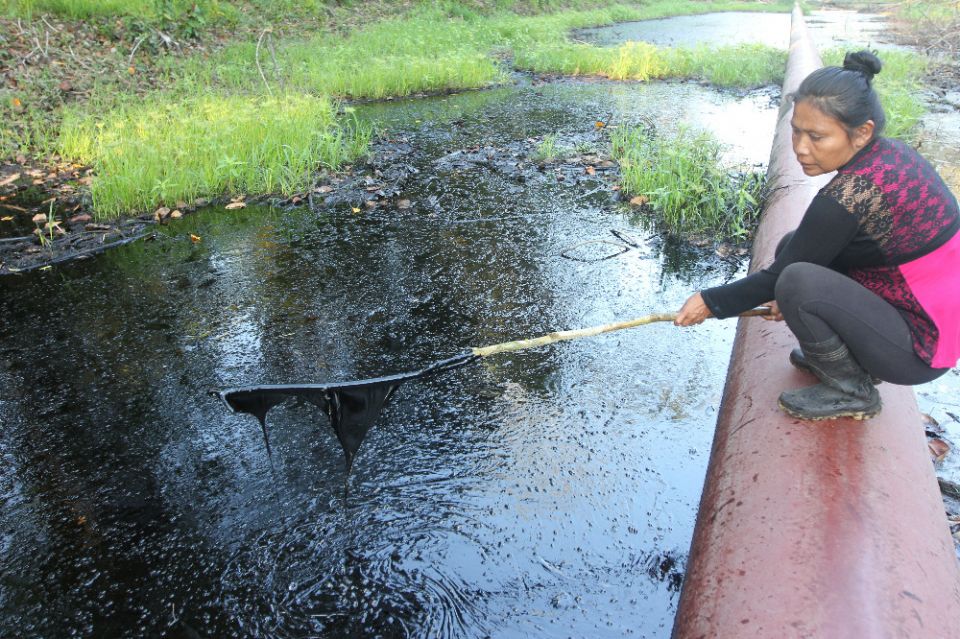 A woman in a community on Peru's Marañón River dips a stick into oil that spilled from a pipeline in August 2016. (Photo by Barbara Fraser)