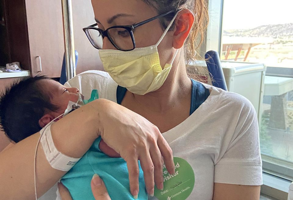 Estefanía Madrigal sits in a wheelchair propped up after her surgery, holding baby Oliver in the neonatal intensive care unit in April 2020 in Lonetree, Colorado. (Courtesy of Estefanía Madrigal)