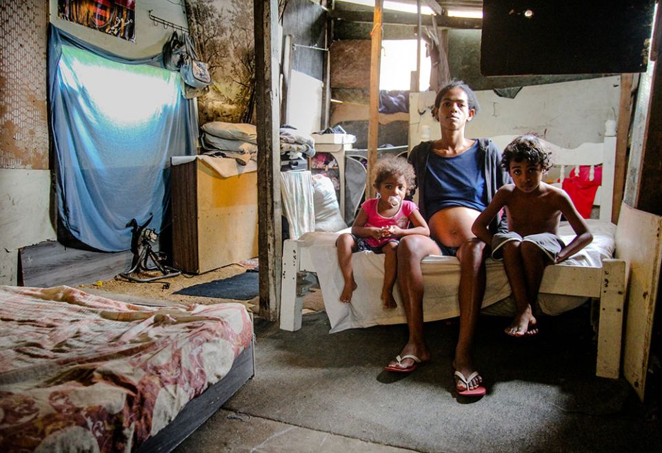 Neilma da Cruz Silva, and two of her children sit on a bed in their tiny wooden house in the Complexo do Alemão, a complex of low-income neighborhoods known as favelas, April 2020 in Rio de Janeiro. (Bruno Itan)