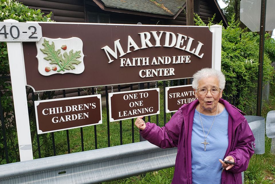 Sr. Verónica Méndez of the Sisters of Our Lady of Christian Doctrine stands beside the sign welcoming visitors to Marydell. (EarthBeat photo/Chris Herlinger)