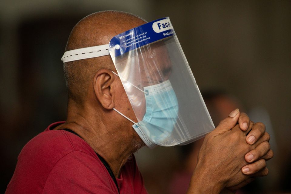 A man wearing a protective mask and face shield prays inside the Minor Basilica of the Black Nazarene in Manila, Philippines, Oct. 2, 2020, during the COVID-19 pandemic. (CNS/Reuters/Eloisa Lopez)