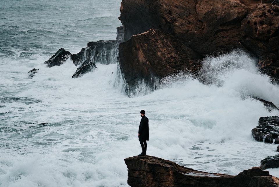 Man standing on rocky shore of Algeria (Unsplash/Benoumechiara)