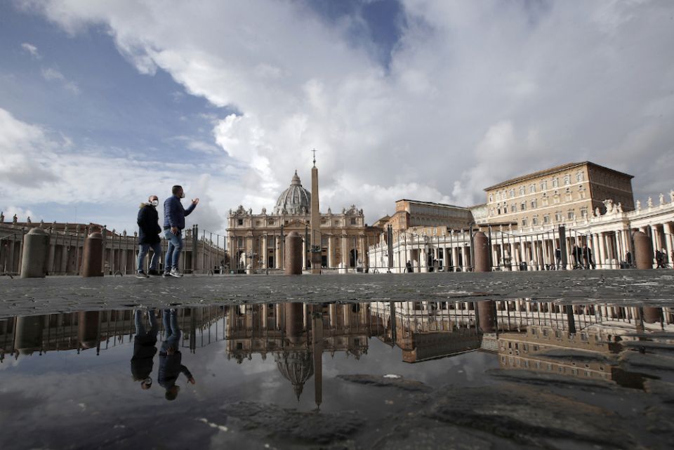 In this Jan. 31, 2021, file photo, people are reflected on a puddle as they walk in St. Peter's Square at the Vatican. (AP/Alessandra Tarantino)