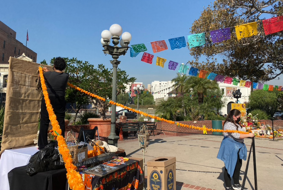 Teresa Velez, left, and her daughter-in-law Olivia Butler, hang marigold garlands on an "ofrenda" in Los Angeles Plaza for a COVID-constrained Día de los Muertos observance. Day of the Dead celebrations have been going on here for more than 30 years. (NCR