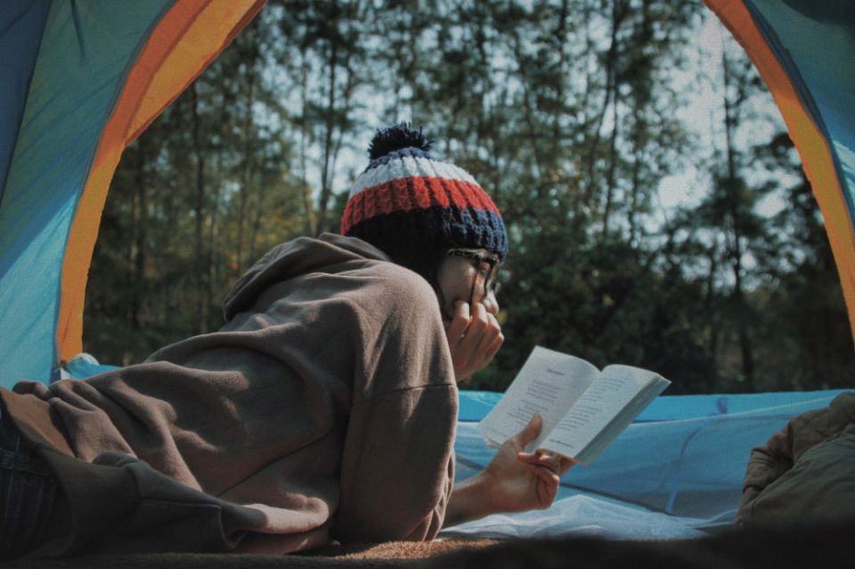 A person reading a book in a tent in the forest. (Unsplash/Lê Tân)