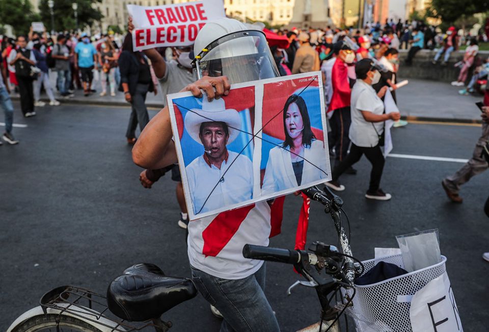 A protester in Lima, Peru, on April 17 holds a sign showing crossed out images of candidates Pedro Castillo and Keiko Fujimori, who will face each other in the second round of Peru's presidential election on June 6. (Newscom/Reuters/Sebastian Castaneda)