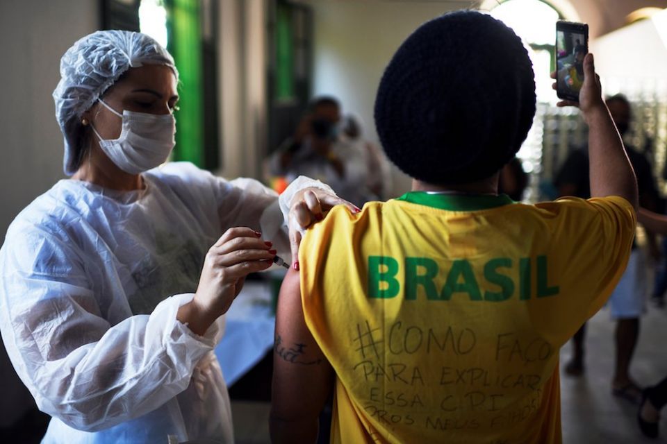 A health care worker administers a dose of Johnson & Johnson COVID-19 vaccine to a resident taking a selfie in Rio de Janeiro July 10. The Brazilian bishops' conference is urging an impartial investigation of government COVID-19 vaccine purchases. (CNS ph