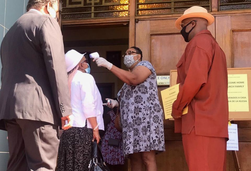 Ganine Arnold takes a visitor’s temperature outside Holy Name of Jesus Church in Los Angeles. (Courtesy of Fr. Kenneth Ugwu)