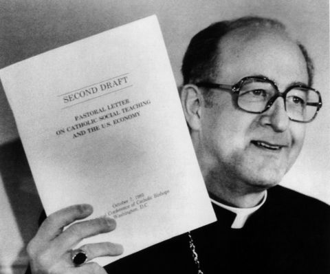 Archbishop Rembert Weakland holds up a copy of the second draft of the U.S. bishops' landmark economic pastoral in this file photo from October 1985. He headed the committee that wrote the pastoral, the final version of which was approved by the U.S. hier