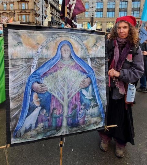 Helen Elwes, a "climate pilgrim" who walked to Glasgow from Bristol, England, holds her handpainted banner depicting Mary embracing a tree of life. (EarthBeat photo/Brian Roewe)