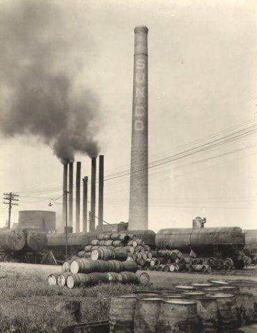 barrels stacked near a Sun Oil Company smokestack