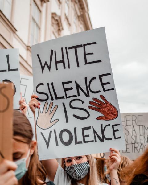 A woman holding a sign that reads "White Silence is Violence" (Unsplash/Simone Fischer)