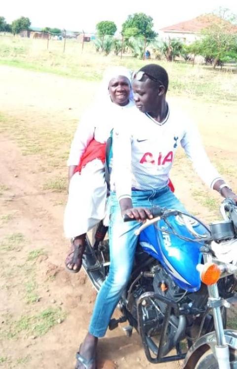 Nun is passenger on motorcycle driven by man in South Sudan.