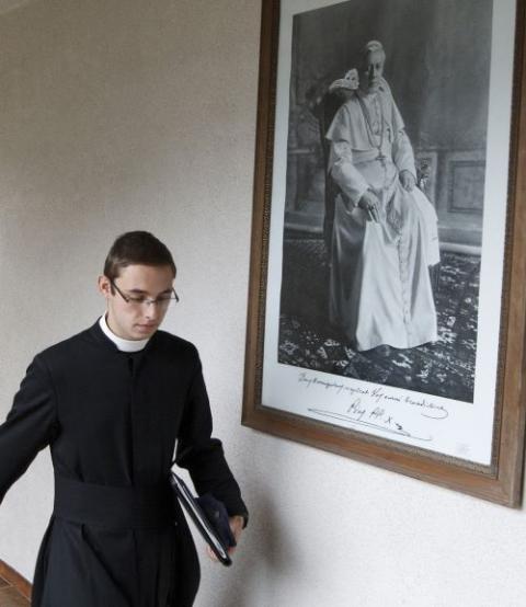 A seminarian walks past a photo of Pope Pius X/