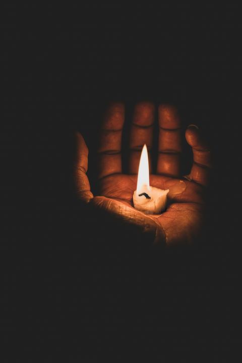 A photo illustration shows a hand holding a small candle in its palm, burning bright against total darkness. (Unsplash/Eyasu Etsub)