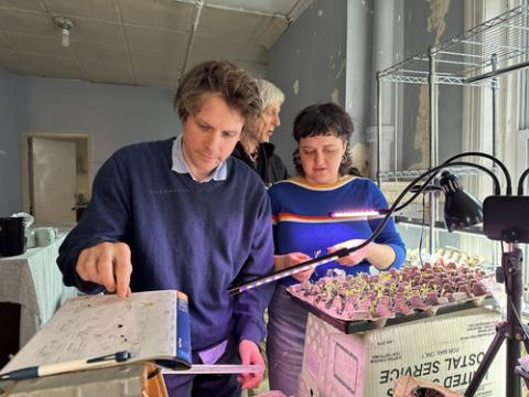 Two people work amongst seedlings, egg cartons, and heat lamps. 