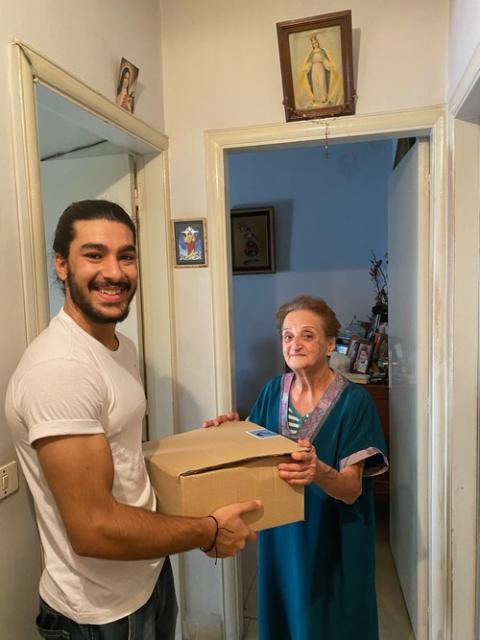 "Teta w Jeddo": Lebanon food ministry for the elderly, 2023. Young man, holding package, smiles alongside elderly woman who stands in her home.
