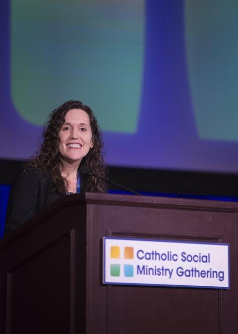 Jill Rauh, newly appointed Executive Director of the USCCB's new Secretariat of Justice and Peace, pictured Jan. 25, 2020. Rauh stands at a podium in front of a screen, smiling. The podium bears a sign reading "Catholic Social Ministry Gathering."