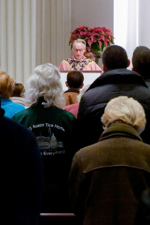 As Debra Tice listens, Jesuit Fr. Jack Dennis reads the Gospel at Mass Dec. 15 at Holy Trinity Church in Washington. (NCR photo/Anthony Peltier)