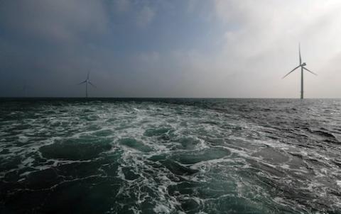 Foamy ocean view offshore of three white wind turbines