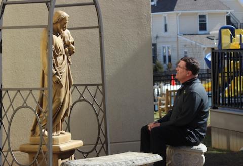 Seated priest looks up at a statue of St. Joseph outside