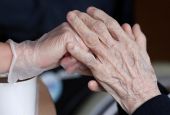 An employee holds the hand of a person at an elderly residence in Brussels April 14, 2020, during the COVID-19 pandemic. (CNS/Reuters/Yves Herman)