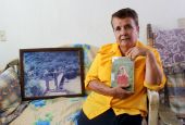 Guadalupe Lara in her home in Guadalajara, Mexico, with a copy of her memoir. A framed photograph of the historic Arcediano Bridge, which was destroyed during dam construction, rests at her side. (Tracy L. Barnett)