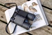 Binoculars sit on a bird field guide book. (Diane Helentjaris/Unsplash/Creative Commons)