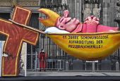 A carnival float depicting a sleeping Cardinal, reading '11 years of relentless processing of cases of abuse' is set in front of the Cologne Cathedral to protest against the Catholic Church in Cologne, Germany, Thursday, March 18, 2021. (AP Photo/Martin M