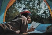A person reading a book in a tent in the forest. (Unsplash/Lê Tân)