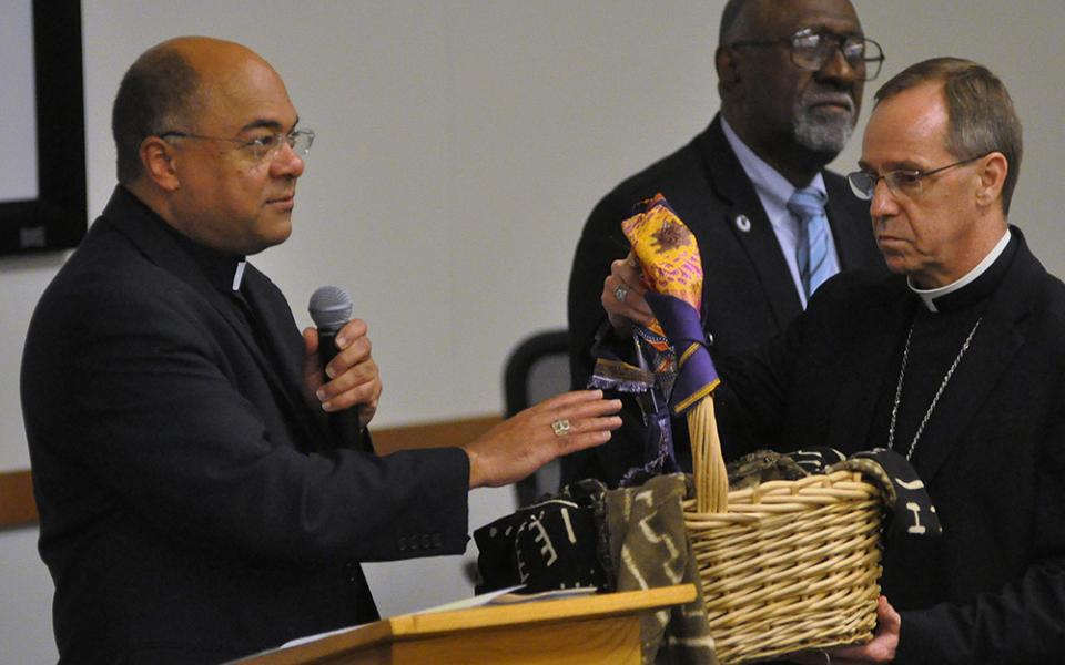 During a 2019 listening session on racism in Indianapolis, Bishop Shelton Fabre of Houma-Thibodaux, Louisiana, blesses a basket (held by Indianapolis Archbishop Charles Thompson) containing people's written accounts of experiences of racism. (CNS)