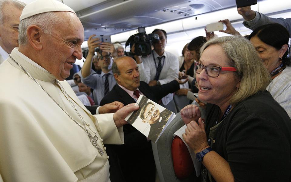 Pope Francis accepts a copy of "Luis Antonio Tagle: Leading by Listening" from Catholic News Service Rome bureau chief Cindy Wooden as he meets journalists aboard his flight from Rome to Havana Sept. 19, 2015. (CNS/Paul Haring)