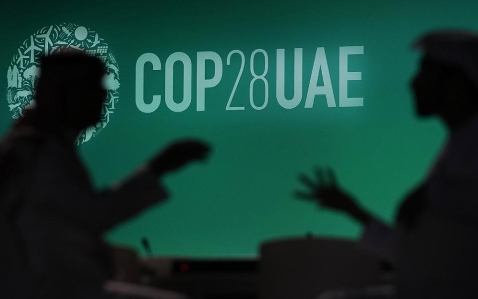 People are silhouetted against a logo for the COP28 U.N. climate summit, Nov. 29, in Dubai, United Arab Emirates. (AP photo/Rafiq Maqbool, File)