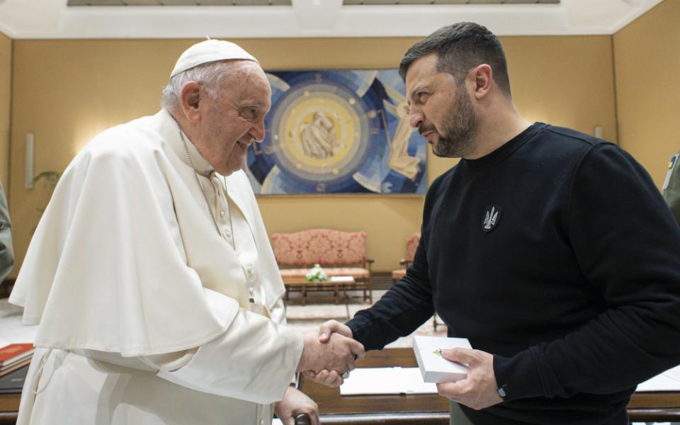 Pope Francis shakes hands with President Volodymyr Zelenskyy shake hands in a yellow room