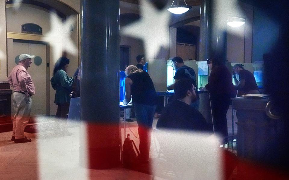 Voters are reflected in a window near an American flag as they mark their ballots during early voting in the general election on Nov. 1, 2024, at City Hall in Providence, R.I. (AP/Steven Senne)