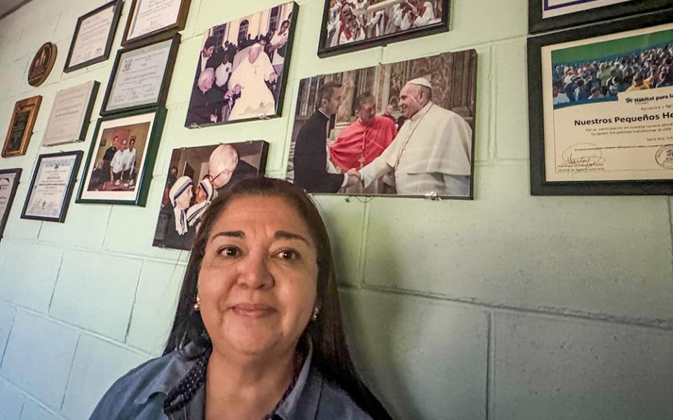 Brenda Méndez, director of programs for Nuestros Pequeños Hermanos in Texistepeque, El Salvador, talks about her time working with New York City Archbishop-elect Ronald Hicks on Jan. 19, 2025, in Texistepeque, with photos of him in the background. Hicks spent five years in El Salvador as the organization's regional director for Central America. Méndez said that he arrived at the site to listen and to support staff. (NCR photo/Rhina Guidos)