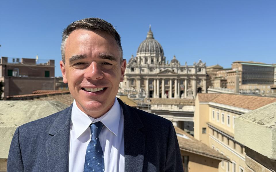 Michael J. O'Loughlin is pictured on the rooftop of the Jesuit Curia, with St. Peter's Basilica in the background, at the Vatican in September 2025. "Capturing the full range of experiences and individuals that make up the church is my goal as editor of NCR," writes O'Loughlin. (Courtesy of Michael J. O'Loughlin)