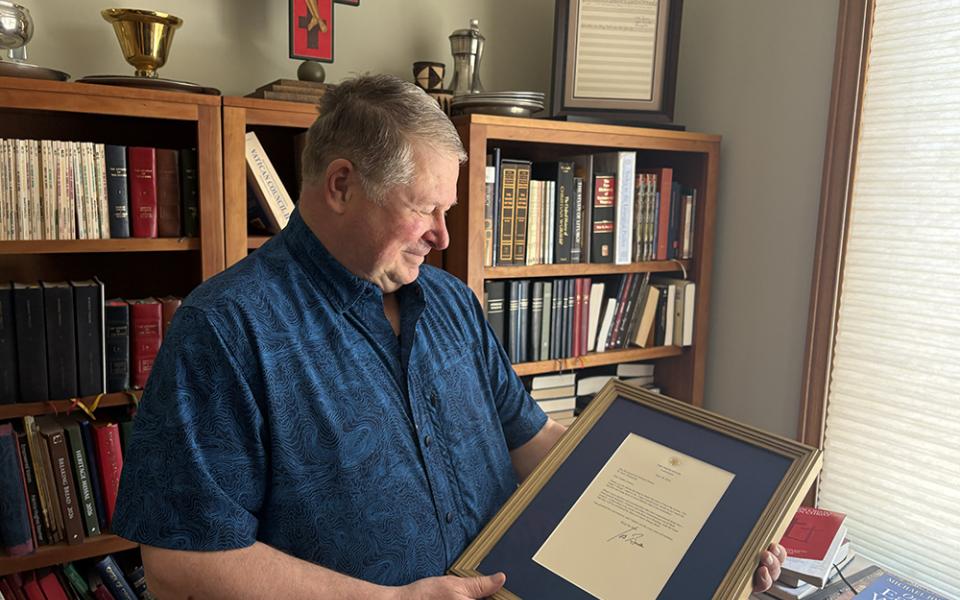 Author, composer and professor Fr. Michael Joncas holding a June 2024 letter from former U.S. president Joe Biden by the bookcase where he framed and displayed the original 1976 score of "On Eagle's Wings," in his apartment in St. Paul, Minnesota, May 2026. (NCR photo/Camillo Barone)