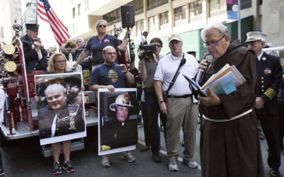 Franciscan Fr. Chris Keenan, chaplain for the New York Fire Department, reads the last homily from Franciscan Fr. Mychal Judge (on poster, center) during the Walk of Remembrance in New York City Sept. 11 this year. (CNS/Octavio Duran)